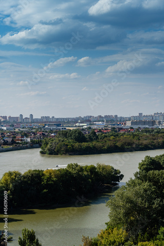 New microdistrict with high-rise residential buildings, shopping centers and new buildings on banks of Kuban River. Trees are overgrown in middle of the river. Krasnodar, Russia - September 05, 2021