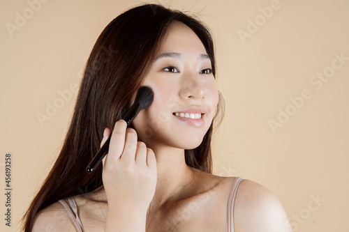 Asian woman with makeup brush on plain background