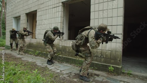 Special forces military group assaulting building, running under windows outdoors, approaching entrance, throwing hand grenade and coming into doorway. Well-coordinated military mission photo