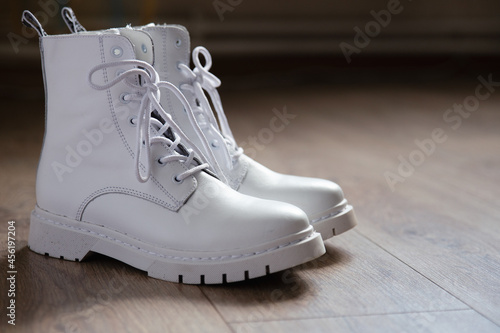 Beautiful pair of high white leather lace-up boots with a massive sole. Set with white stylish shoes on the floor. The trend of the season: the brightness and uniqueness the image