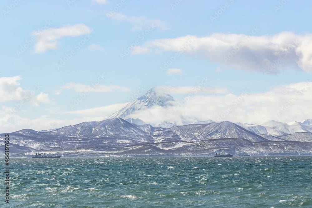Russia, Kamchatka. Ships in the cold waters of the Avacha Bay. There are icy, snow-covered mountains and volcanoes in the background.
