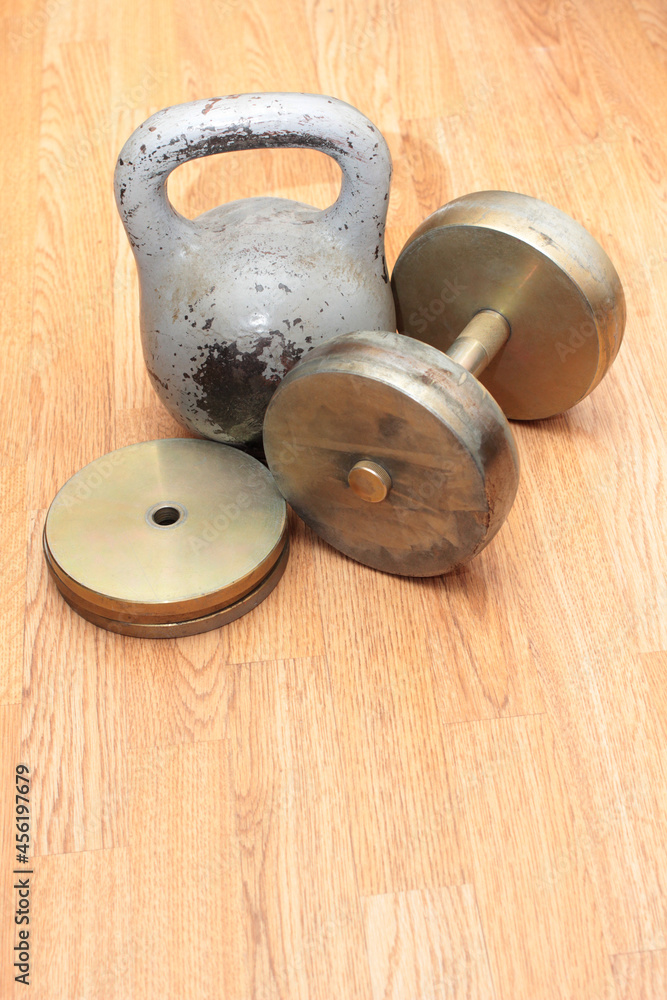 Heavy metal dumbbells and weights on wooden floor Heavy metal dumbbells and weights on wooden floor