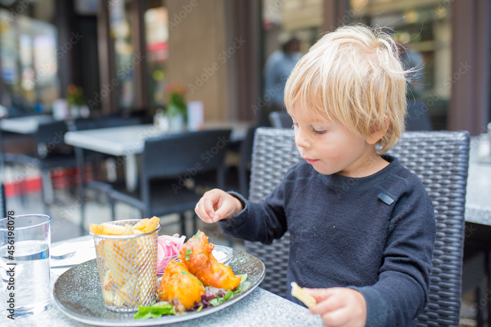 Preschool child, cute boy, eating fish and chips a restaurant, cozy atmosphere, local small restaurant in Stockholm