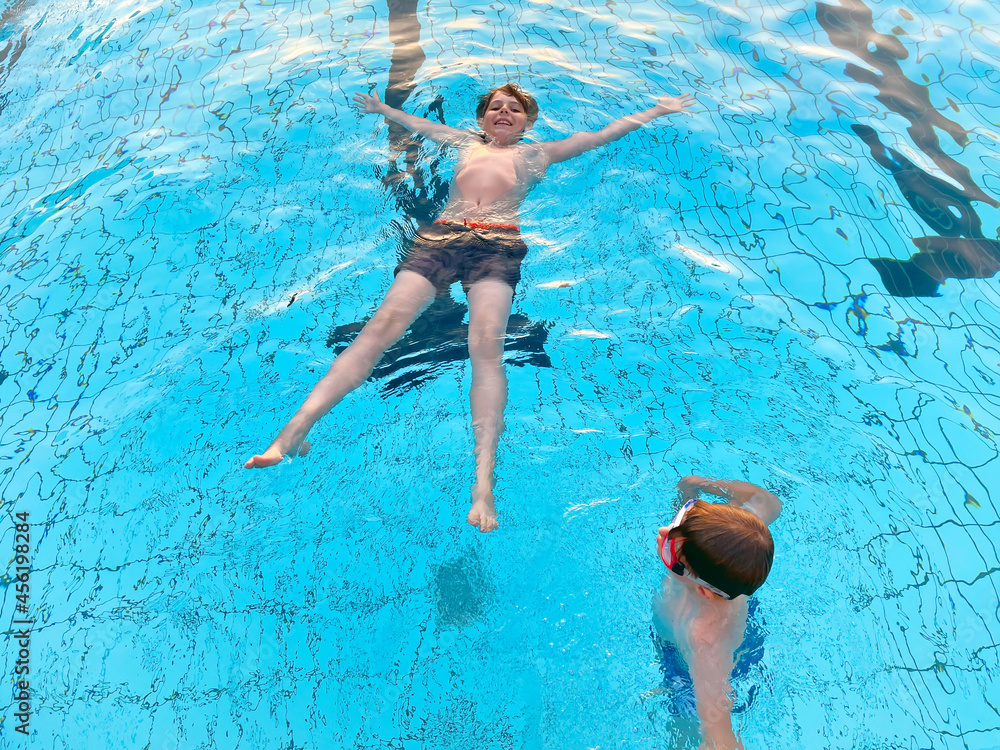 Two school kids boys playing and splashing in an outdoor swimming pool on warm summer day. Happy healthy children enjoying sunny weather in city public pool. Kids activity outdoors with water.