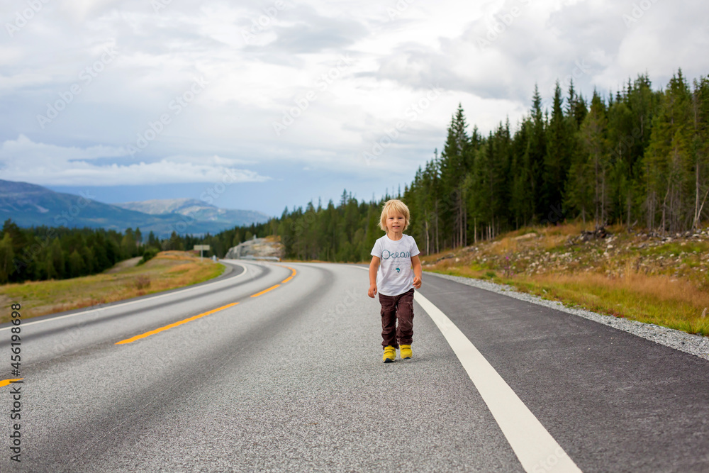 Beautiful blond child, standing in the middle of the highway on an empty road, running happily, enjoying the beautiful landscape of Norway