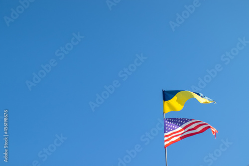 Ukrainian and American flag on a blue sky background. Friendship of peoples and diplomatic mission. Yellow-blue and stars-striped fabric on a flagpole.