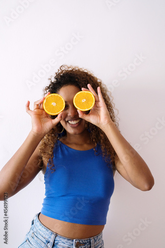 Black woman with curly hair holding cut orange halves in front of her eyes having fun