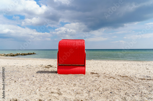 Fototapeta Naklejka Na Ścianę i Meble -  Traditional German roofed wicker beach chairs on the beach of Baltic Sea. Beach with red chairs on stormy sunny day. Ostsee.
