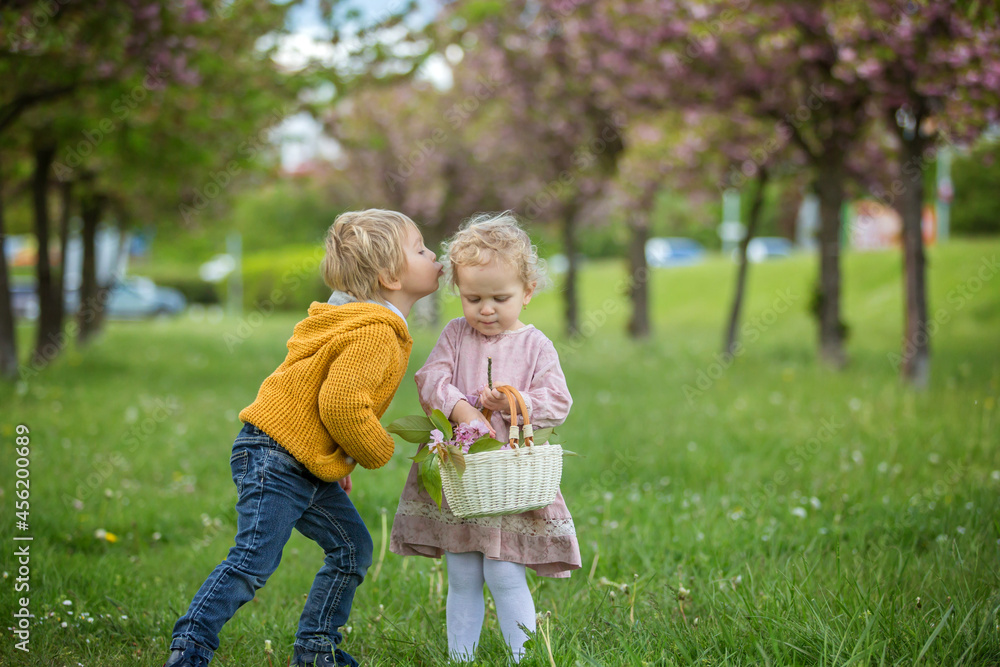 Beautiful children, toddler boy and girl, playing together in cherry blossom garden,boy giving a little bouquet of wild flowers to the girl. Kids friendship Beautiful children, toddler boy and girl, playing together in cherry blossom garden,boy giving a little bouquet of wild flowers to the girl. Kids friendship