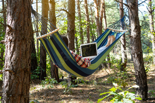 Freelance and working at nature. Freelancer woman works at notebook while lying on the hammock in the forest. Online business independent of the office.