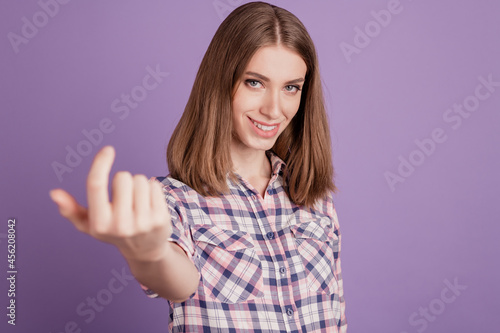 Portrait of smiling positive girl making beckoning gesture with finger inviting isolated over violet background