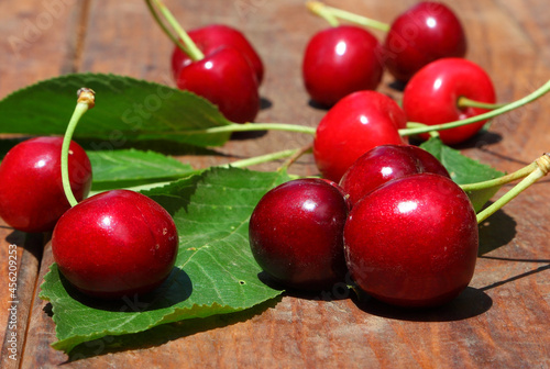Ripe red sweet cherry with green leaves on the rough wooden background