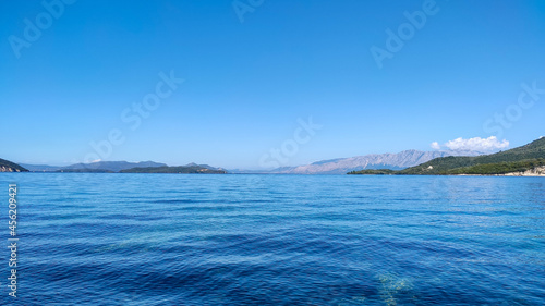 Blue clear calm Ionian Sea water with clear sky and green hills in distance. Panoramic view of Lefkada island coast in Greece. Summer vacation idyllic travel destination