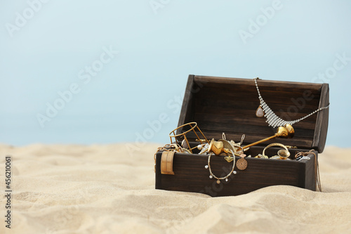 Open wooden chest with treasures on sandy beach, space for text