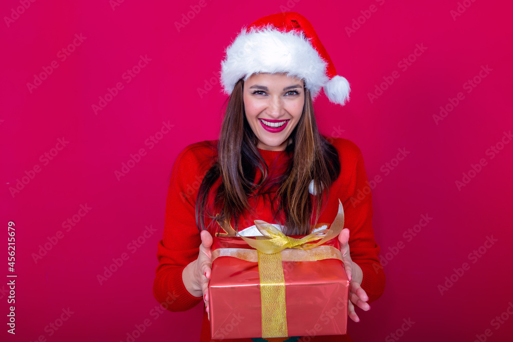 beautiful woman in red sweater and Santa Claus hat offering a gift with a big smile beautiful woman in red sweater and Santa Claus hat offering a gift with a big smile