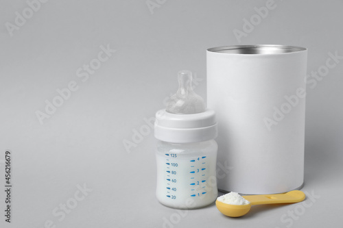 Fotografie, Obraz Blank can of powdered infant formula with scoop and feeding bottle on light grey background, space for text