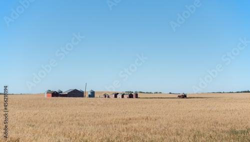 Granaries, silos, farm buildings and an abandoned tractor in the middle of a field of oats in late summer on the prairies of Saskatchewan, Canada. photo