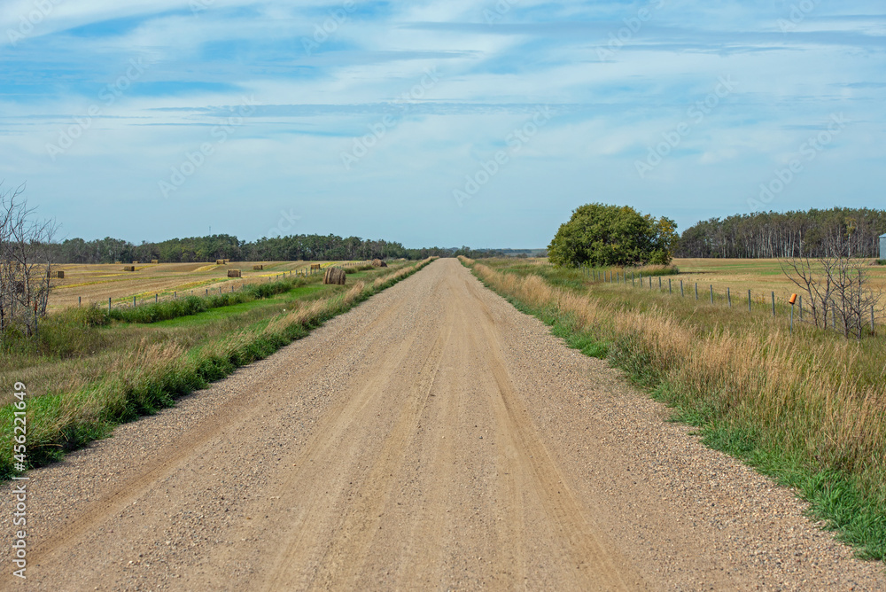 A gravel road along a field of bales in the prairies of rural Saskatchewan, Canada.
