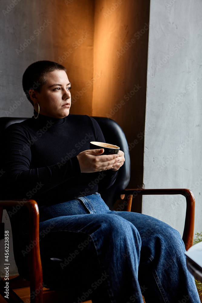 A young girl with glasses, with short hair and a nose piercing is sitting in a cafe, drinks coffee. A young girl with glasses, with short hair and a nose piercing is sitting in a cafe, drinks coffee.