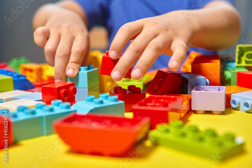 A beautiful boy is playing at home with building blocks. A cute smiling boy is playing with a constructor with a lot of colorful plastic blocks in the room  building a city. Preschool classes.
