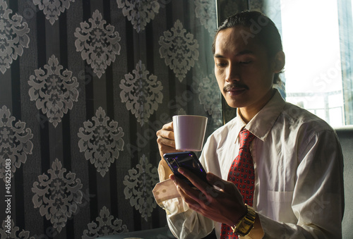 Professional Asian Man drinking coffee while using a cell phone for work