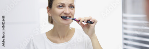 Smiling woman brushes her teeth in front of mirror