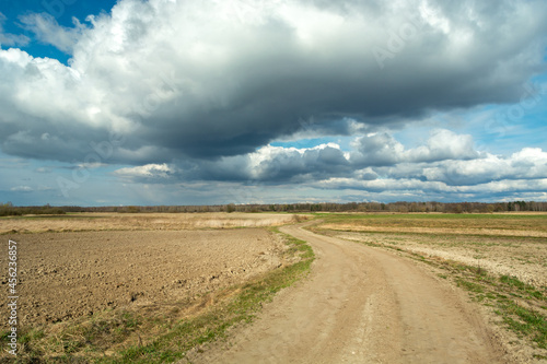 A sandy road through the fields and clouds on the sky