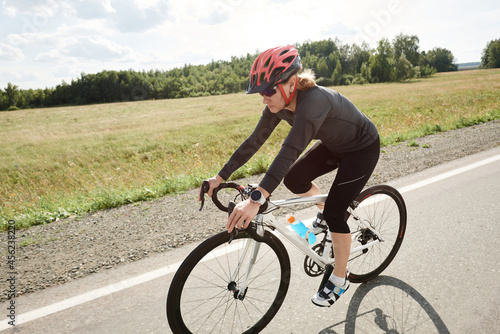 Female cyclist in sports clothing and in helmet riding a racing bike on road