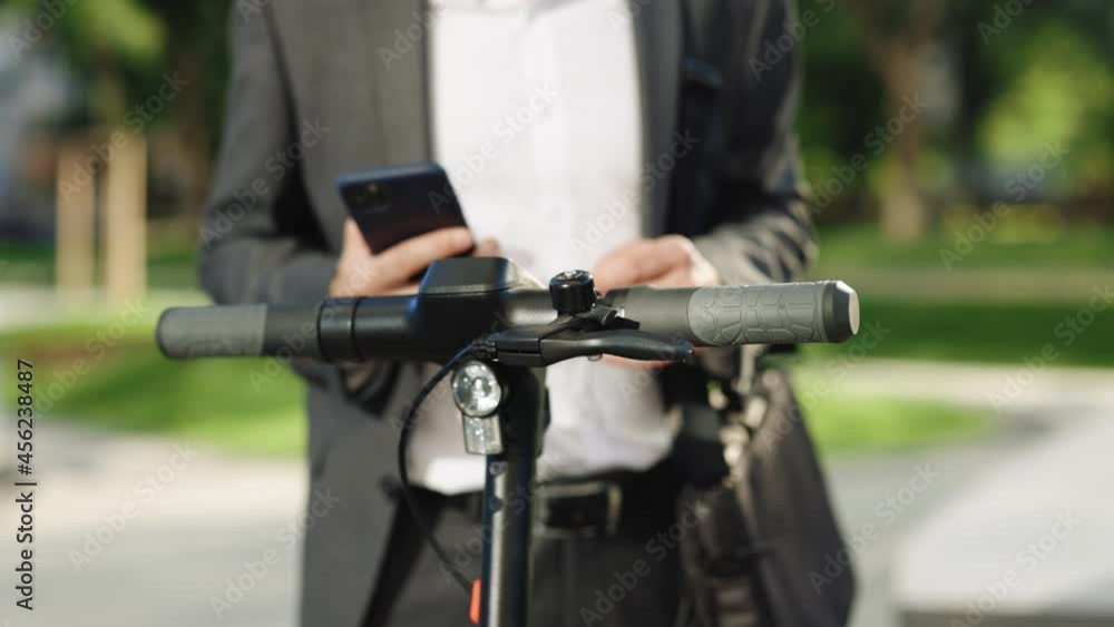 Unknown businessman in classic suit is coming up to an electric scooter and using mobile phone app. Man rents electric scooter. Eco-friendly transportation. Outdoors of business center Unknown businessman in classic suit is coming up to an electric scooter and using mobile phone app. Man rents electric scooter. Eco-friendly transportation. Outdoors of business center