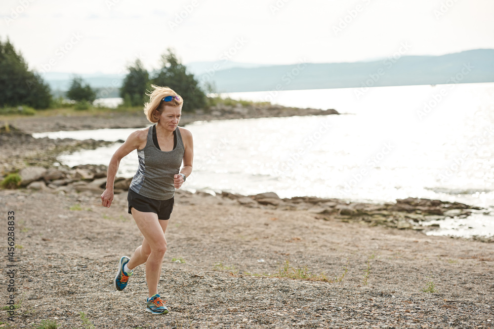 Young female athlete in sportswear running along the lakeshore in the morning