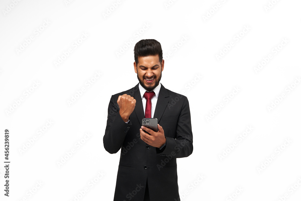 Portrait of young indian manager using his mobile phone and celebrating the victory on white isolated background Portrait of young indian manager using his mobile phone and celebrating the victory on white isolated background