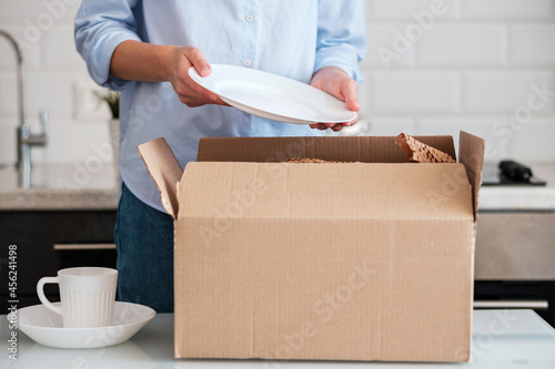 A woman unpacks a box with new dishes.