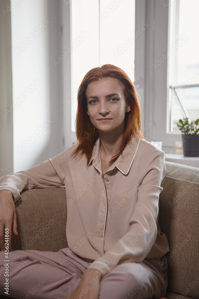 Caucasian young good looking woman with red hair sitting on the sofa in room and Woman looking at camera, smiling and laughing. Joy, warmth, happiness. Caucasian young good looking woman with red hair sitting on the sofa in room and Woman looking at camera, smiling and laughing. Joy, warmth, happiness.