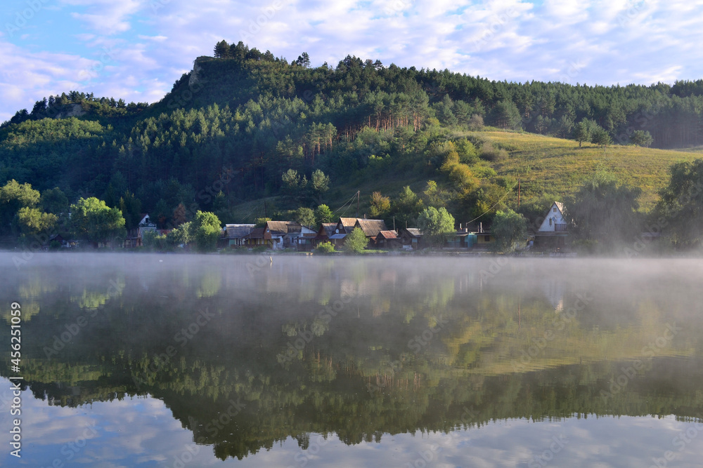 Waterfront houses by the misty lake. Between hills at summer dawn. Arló, Hungary Waterfront houses by the misty lake. Between hills at summer dawn. Arló, Hungary