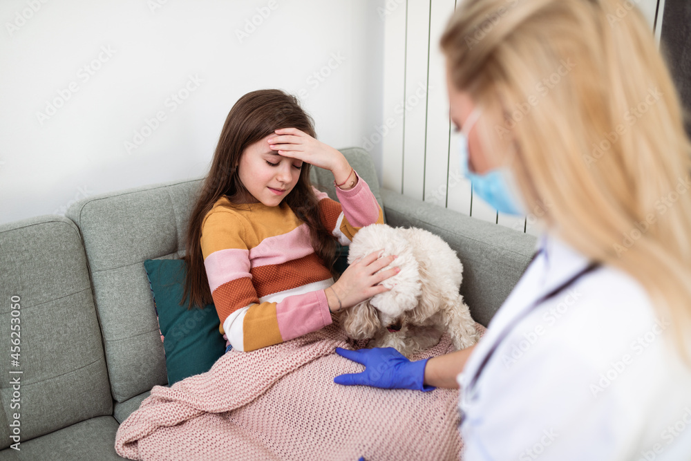 Cute sick little school girl lying on living room sofa and her doctor