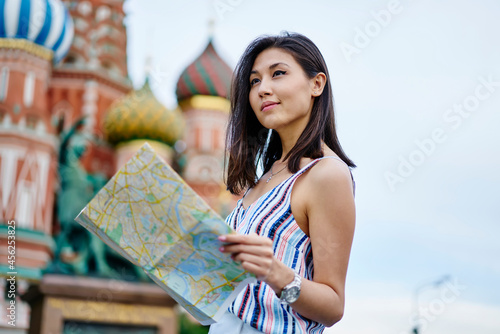 Contemplative Asian tourist with travel map thinking about route direction during summer vacations, pondering female with location paper visiting historis city during international journey trip photo