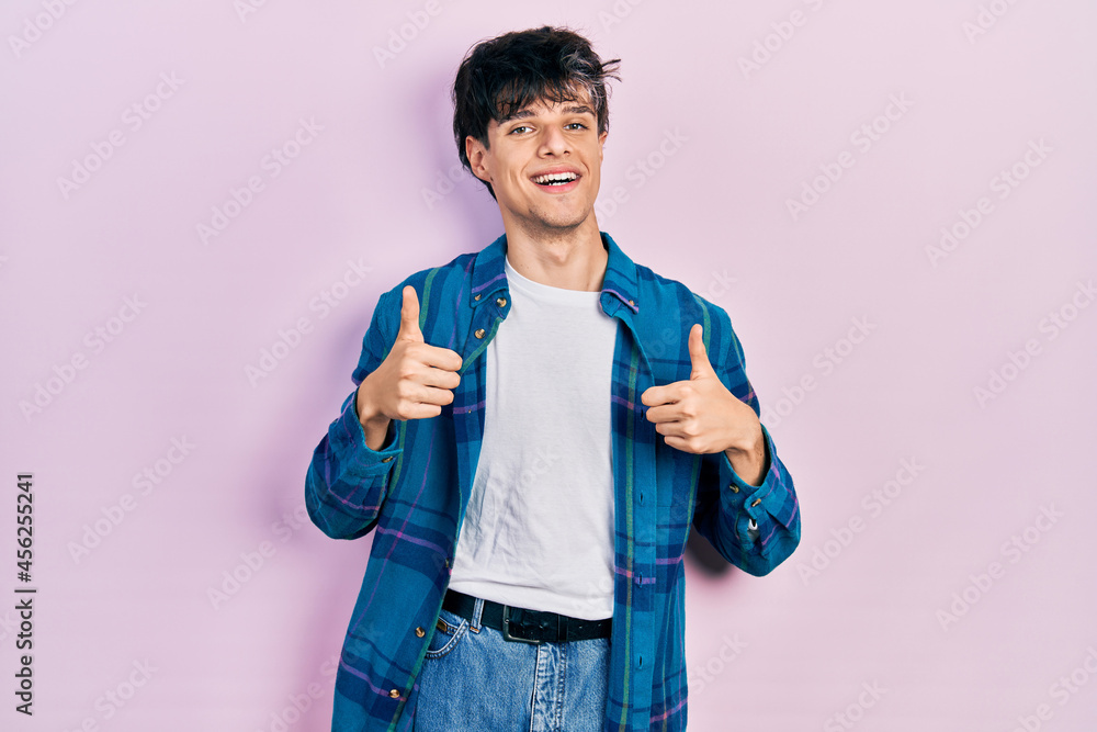 Handsome hipster young man wearing casual white t shirt and vintage shirt success sign doing positive gesture with hand, thumbs up smiling and happy. cheerful expression and winner gesture. Handsome hipster young man wearing casual white t shirt and vintage shirt success sign doing positive gesture with hand, thumbs up smiling and happy. cheerful expression and winner gesture.