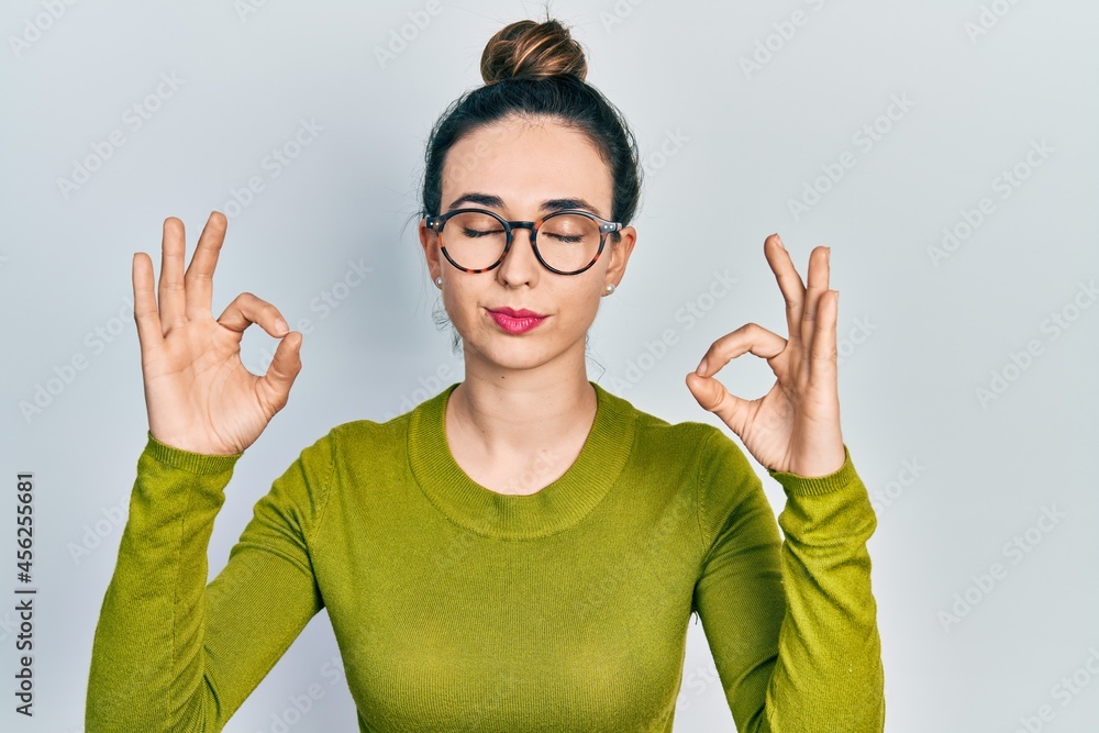Young hispanic girl wearing casual clothes and glasses relax and smiling with eyes closed doing meditation gesture with fingers. yoga concept.