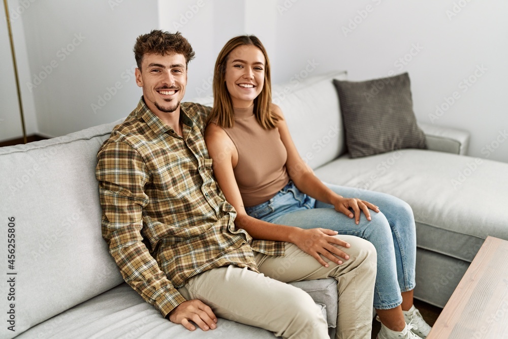 Young hispanic couple smiling happy and hugging sitting on the sofa at home.
