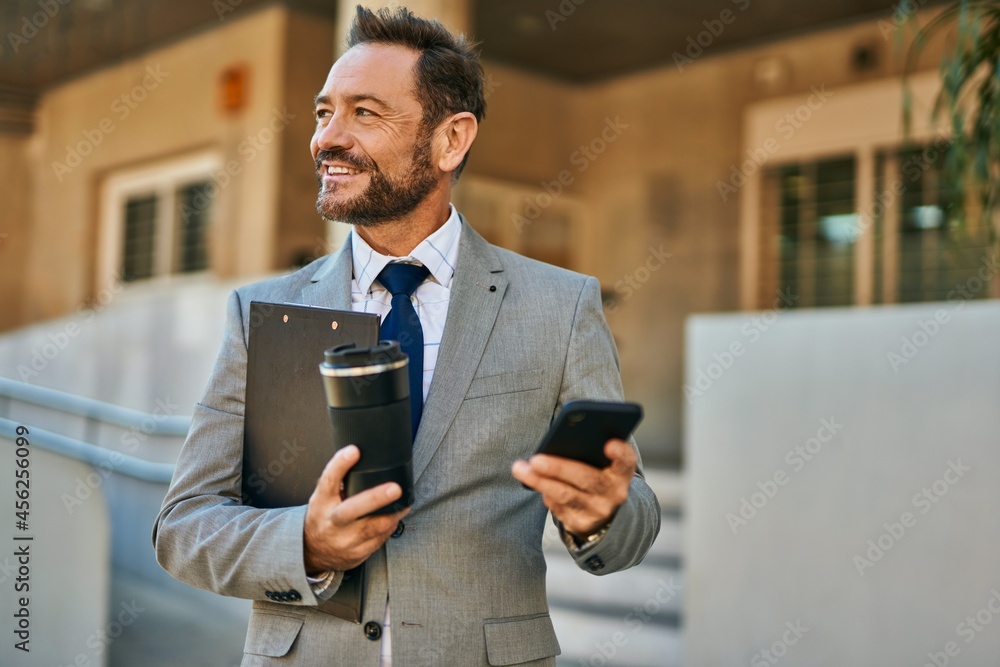 Middle age businessman using smartphone and drinking coffee at the city.