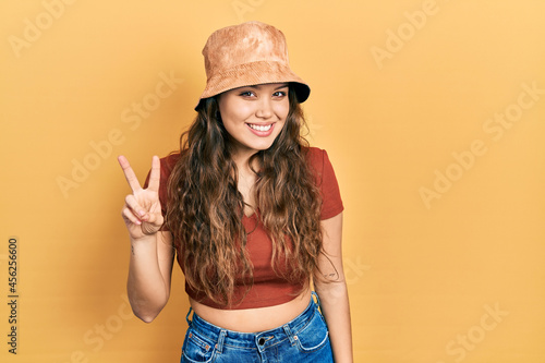 Young hispanic girl wearing casual clothes and hat showing and pointing up with fingers number two while smiling confident and happy.