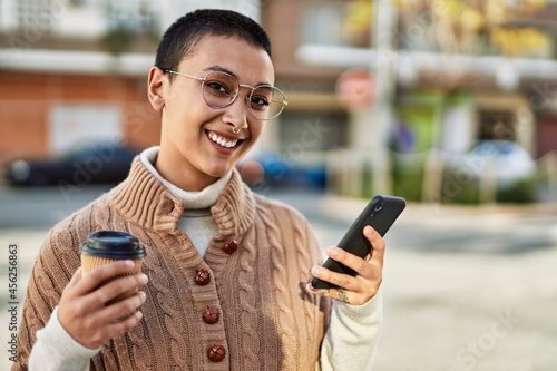 Young hispanic woman with short hair smiling happy drinking a cup of coffee and using smartphone