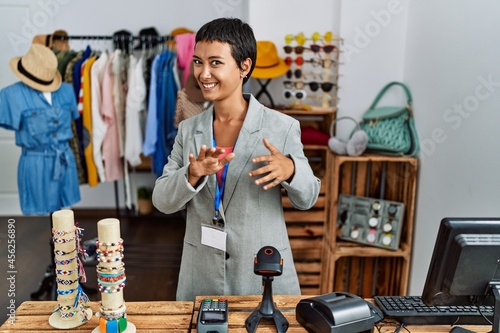 Young hispanic woman with short hair working as manager at retail boutique disgusted expression, displeased and fearful doing disgust face because aversion reaction. with hands raised