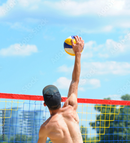 Beach volleyball. Male volley player hitting ball over the net attacking photo