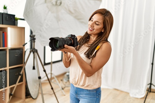 Young hispanic photographer woman smiling happy using camera at photo studio.
