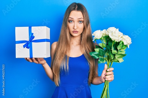 Young blonde girl holding anniversary present and bouquet of flowers skeptic and nervous, frowning upset because of problem. negative person.