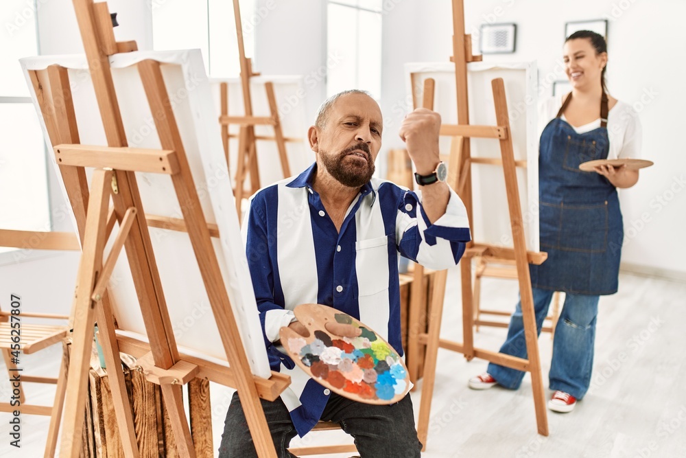 Senior artist man at art studio angry and mad raising fist frustrated and furious while shouting with anger. rage and aggressive concept. Senior artist man at art studio angry and mad raising fist frustrated and furious while shouting with anger. rage and aggressive concept.