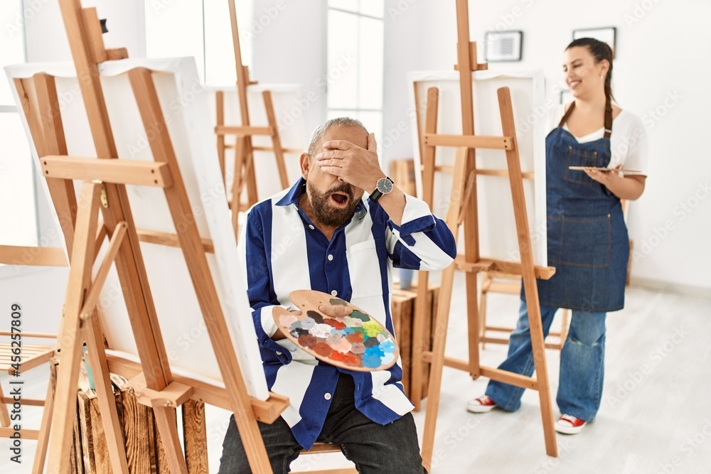 Senior artist man at art studio smiling and laughing with hand on face covering eyes for surprise. blind concept. Senior artist man at art studio smiling and laughing with hand on face covering eyes for surprise. blind concept.
