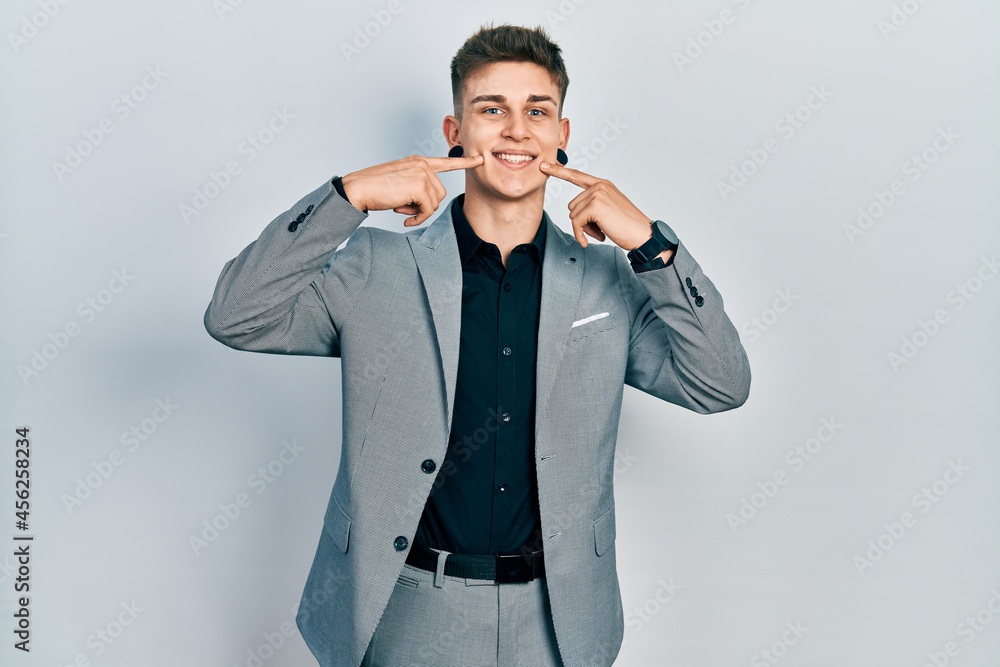 Young caucasian boy with ears dilation wearing business jacket smiling cheerful showing and pointing with fingers teeth and mouth. dental health concept. Young caucasian boy with ears dilation wearing business jacket smiling cheerful showing and pointing with fingers teeth and mouth. dental health concept.