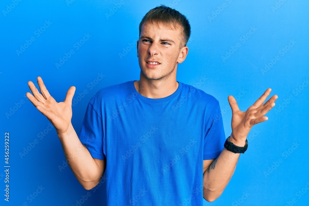 Young caucasian man wearing casual blue t shirt crazy and mad shouting and yelling with aggressive expression and arms raised. frustration concept. Young caucasian man wearing casual blue t shirt crazy and mad shouting and yelling with aggressive expression and arms raised. frustration concept.